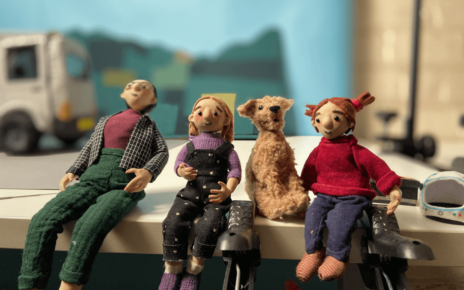 four characters sitting side by side from the fostering network animation. A woman, two girls and a dog , with a car in the background.
