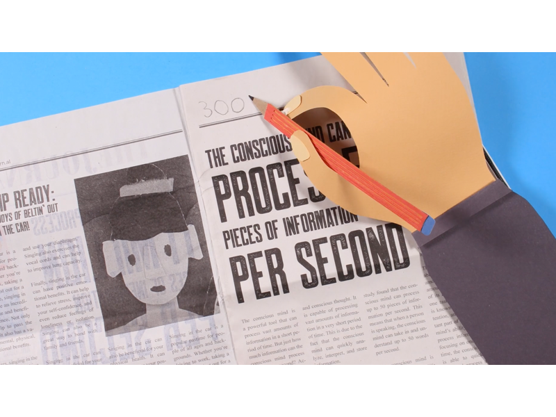 A still image from a stop motion animation. Showing a papercrafted hand , holding a pencil and drawing on a newspaper.