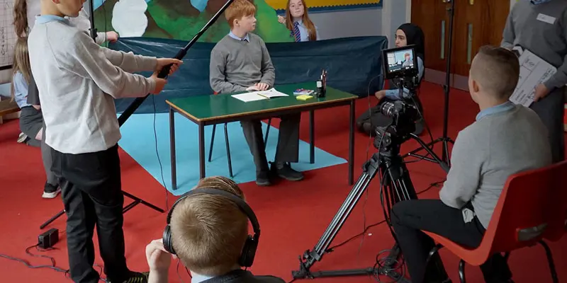 a group of school students create a film in front of a handmade mountain landscape background