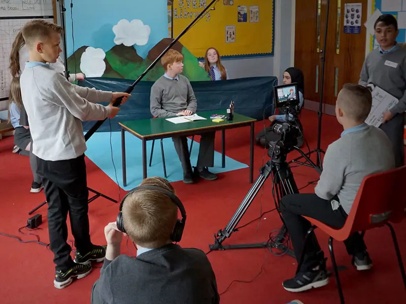 a group of school students create a film in front of a handmade mountain landscape background